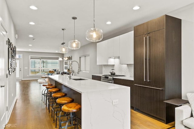 kitchen featuring decorative backsplash, high end stove, sink, a center island with sink, and white cabinetry