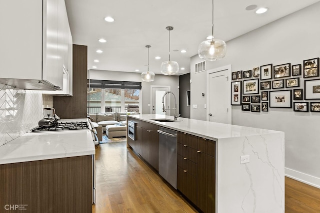 kitchen featuring dark brown cabinetry, sink, dishwasher, decorative light fixtures, and a kitchen island with sink