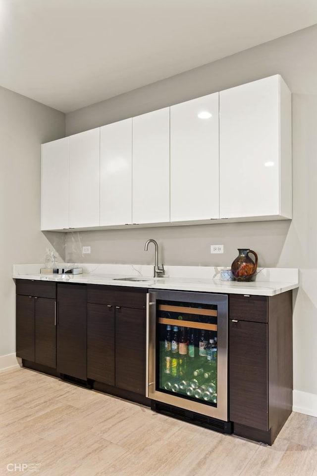 bar featuring dark brown cabinetry, white cabinetry, beverage cooler, and sink