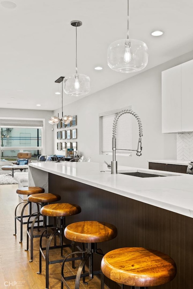 bar featuring backsplash, sink, decorative light fixtures, white cabinets, and light hardwood / wood-style floors