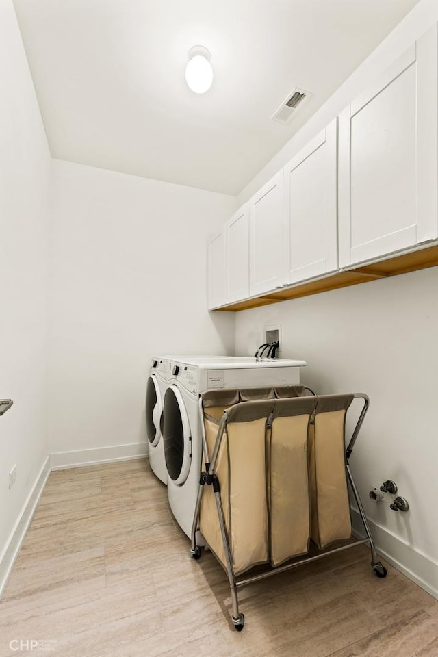 clothes washing area with washing machine and dryer, cabinets, and light hardwood / wood-style floors