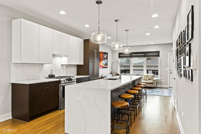 kitchen with dark brown cabinets, sink, light hardwood / wood-style flooring, stainless steel gas stove, and an island with sink