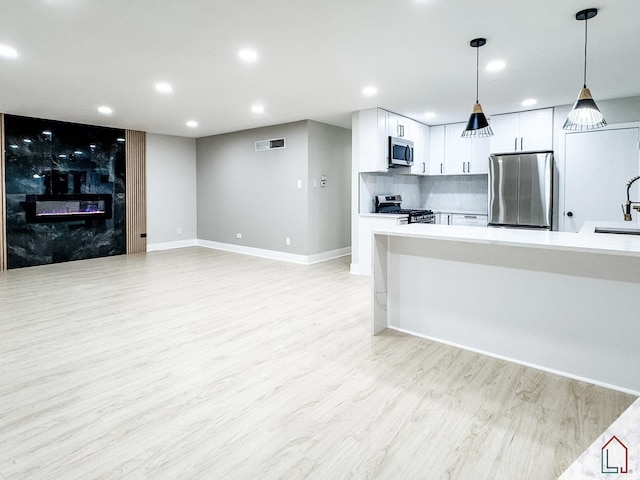 kitchen with appliances with stainless steel finishes, backsplash, pendant lighting, white cabinets, and light hardwood / wood-style floors