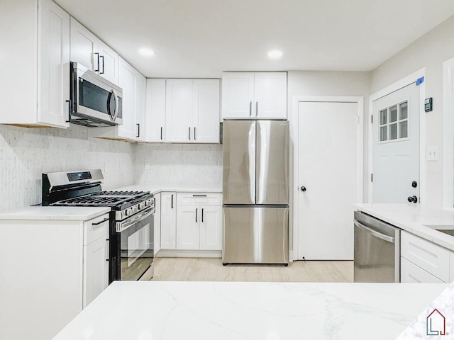 kitchen with light stone countertops, appliances with stainless steel finishes, backsplash, light wood-type flooring, and white cabinetry