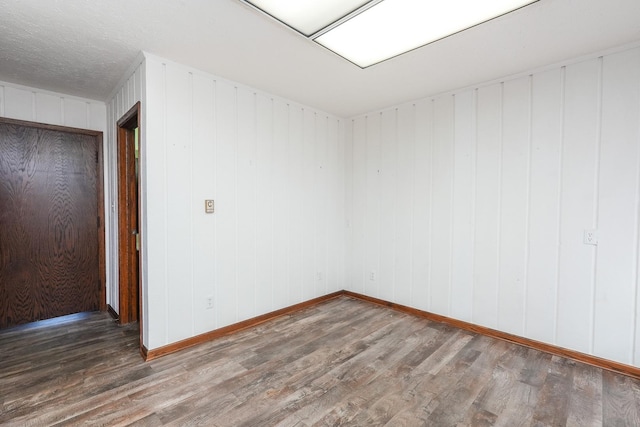 spare room featuring wooden walls, wood-type flooring, and a textured ceiling