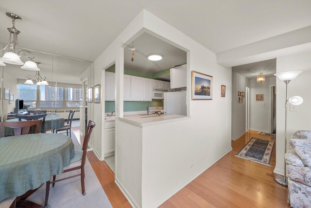 kitchen featuring hanging light fixtures, light hardwood / wood-style flooring, kitchen peninsula, white appliances, and white cabinets