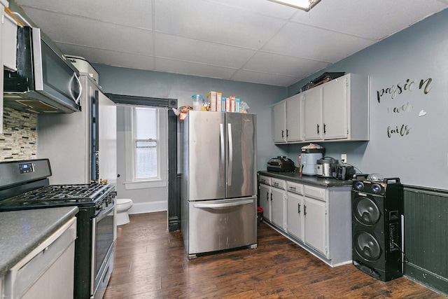 kitchen with a drop ceiling, white cabinets, dark wood-type flooring, and appliances with stainless steel finishes