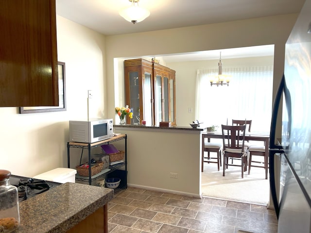 kitchen with black refrigerator, hanging light fixtures, a notable chandelier, and kitchen peninsula