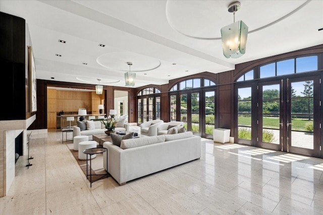 living room with french doors, a tray ceiling, and wooden walls