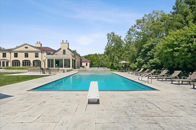 view of swimming pool featuring a patio, a diving board, and a sunroom