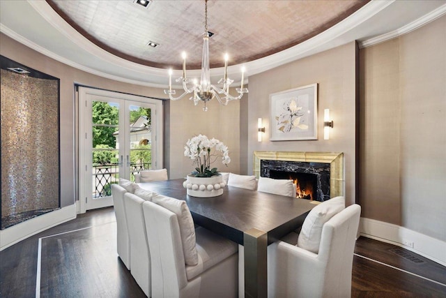 dining space with french doors, dark hardwood / wood-style flooring, ornamental molding, a tray ceiling, and a premium fireplace