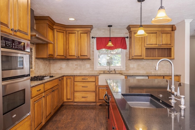 kitchen with pendant lighting, sink, wall chimney range hood, and stainless steel appliances