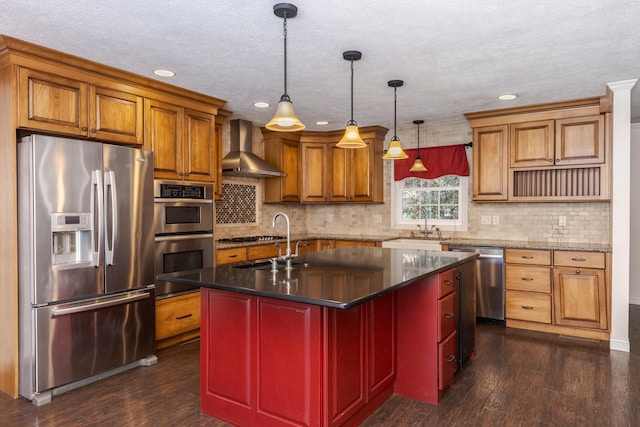 kitchen with wall chimney exhaust hood, hanging light fixtures, dark hardwood / wood-style flooring, a center island with sink, and appliances with stainless steel finishes