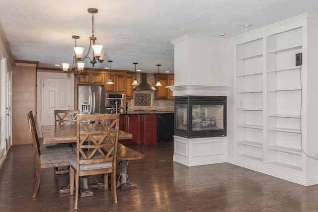 dining area with a multi sided fireplace, dark hardwood / wood-style floors, ornamental molding, built in features, and a notable chandelier