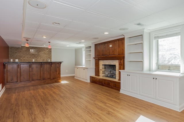 unfurnished living room featuring built in shelves, light hardwood / wood-style flooring, brick wall, and ornamental molding