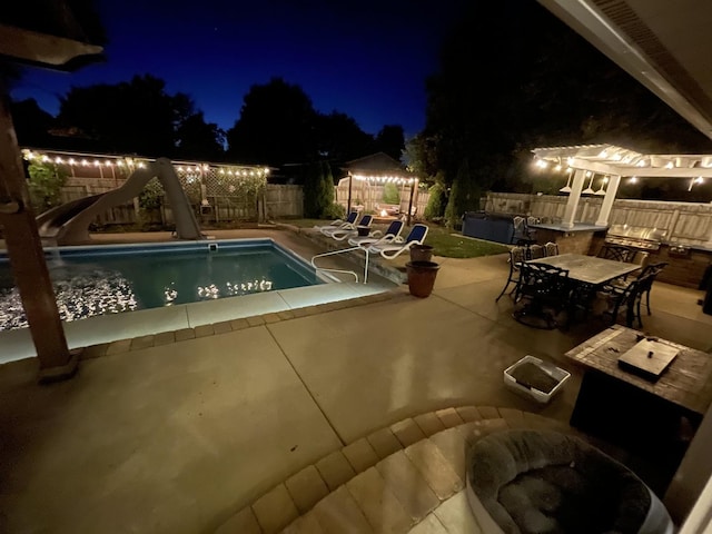 pool at night with a patio area and a water slide