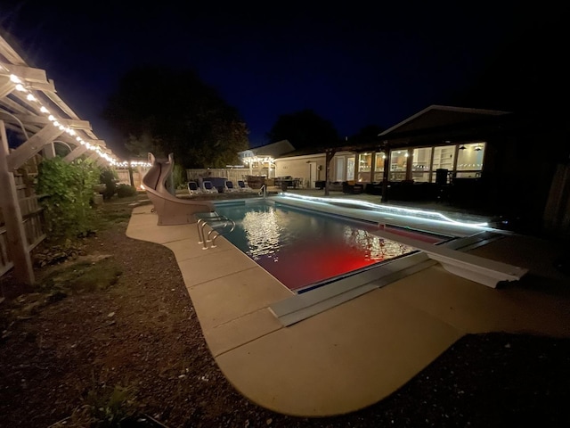 pool at night featuring a patio and a water slide