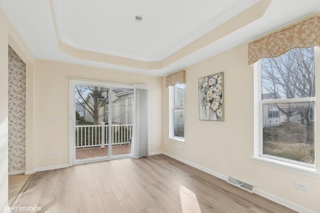 spare room with a raised ceiling, crown molding, plenty of natural light, and light hardwood / wood-style flooring