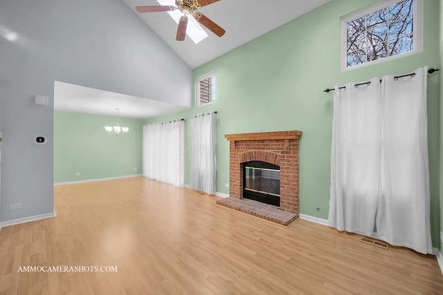 unfurnished living room featuring ceiling fan with notable chandelier, light wood-type flooring, high vaulted ceiling, and a brick fireplace