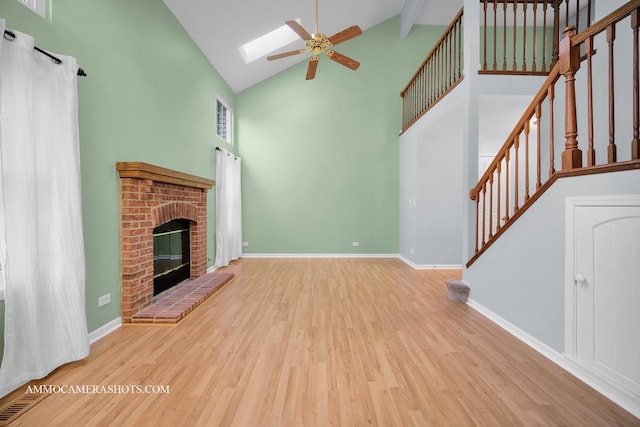 unfurnished living room featuring a skylight, light hardwood / wood-style flooring, high vaulted ceiling, and a brick fireplace