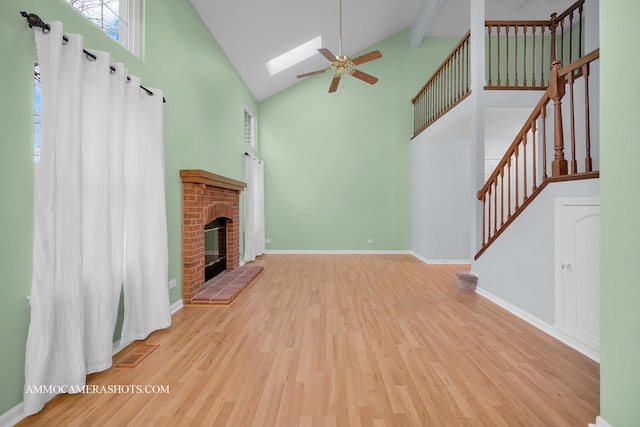 unfurnished living room with a skylight, ceiling fan, high vaulted ceiling, a fireplace, and light wood-type flooring