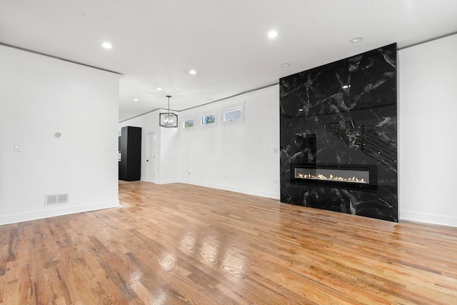 unfurnished living room featuring light wood-type flooring, crown molding, and a high end fireplace