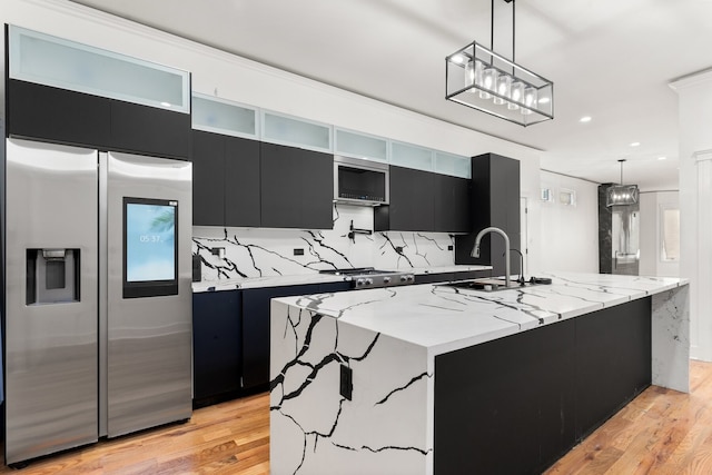 kitchen featuring sink, stainless steel fridge, an island with sink, pendant lighting, and light hardwood / wood-style floors