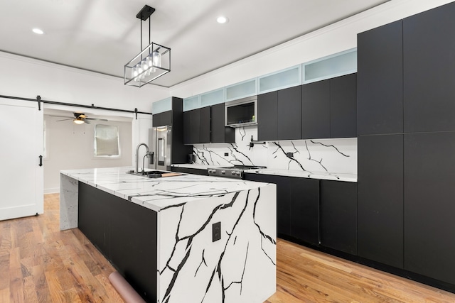 kitchen featuring backsplash, sink, a barn door, a center island with sink, and hanging light fixtures