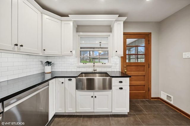 kitchen featuring sink, tasteful backsplash, dark tile patterned floors, stainless steel dishwasher, and white cabinets