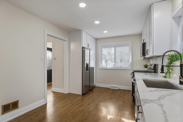 kitchen featuring light stone countertops, appliances with stainless steel finishes, dark hardwood / wood-style flooring, sink, and white cabinets