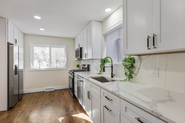 kitchen featuring light stone countertops, sink, backsplash, white cabinets, and appliances with stainless steel finishes