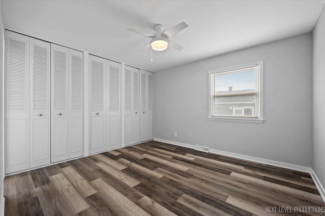 unfurnished bedroom featuring ceiling fan, dark wood-type flooring, and two closets