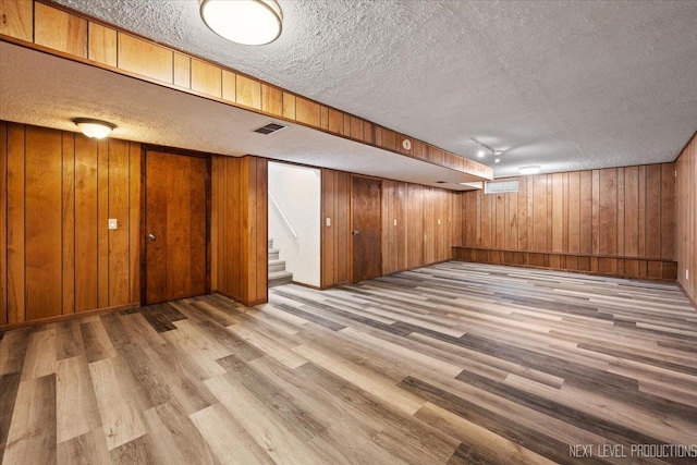 basement with wood walls, light hardwood / wood-style floors, a textured ceiling, and track lighting