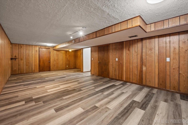 basement with a textured ceiling, wood walls, and rail lighting