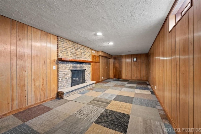 unfurnished living room with a textured ceiling, carpet flooring, a fireplace, and wooden walls