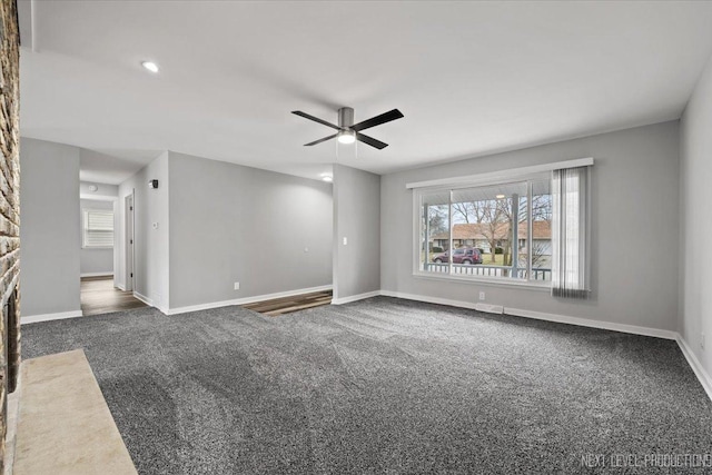 spare room featuring dark colored carpet, ceiling fan, and a fireplace