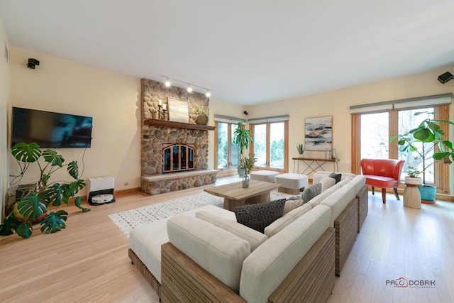 living room featuring plenty of natural light, a stone fireplace, light wood-type flooring, and track lighting