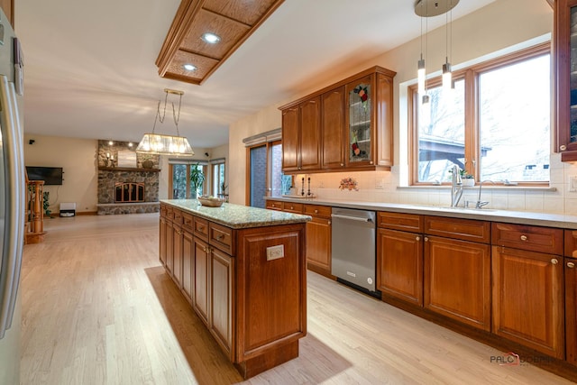 kitchen featuring pendant lighting, stainless steel dishwasher, light wood-type flooring, a fireplace, and a kitchen island