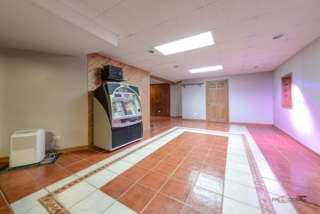 basement featuring tile patterned flooring, a paneled ceiling, and wooden walls