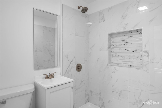 bathroom with a tile shower, vanity, and toilet