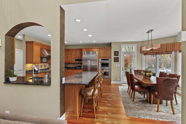 kitchen featuring sink, light hardwood / wood-style flooring, appliances with stainless steel finishes, pendant lighting, and wall chimney range hood