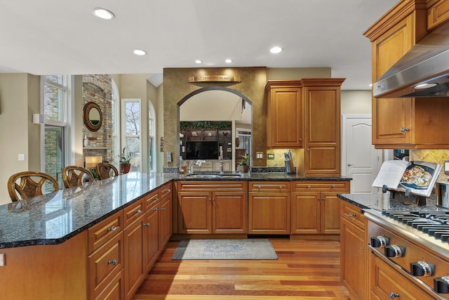 kitchen with dark stone counters, kitchen peninsula, light hardwood / wood-style floors, and exhaust hood