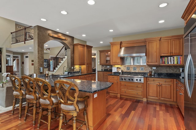 kitchen featuring a breakfast bar, ventilation hood, dark hardwood / wood-style floors, kitchen peninsula, and stainless steel appliances