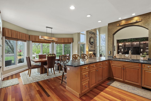 kitchen featuring sink, dark stone countertops, hanging light fixtures, light hardwood / wood-style floors, and kitchen peninsula