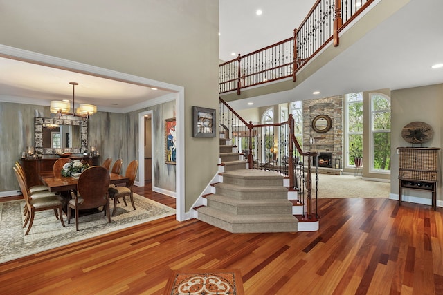 entryway featuring a towering ceiling, ornamental molding, a fireplace, and wood-type flooring