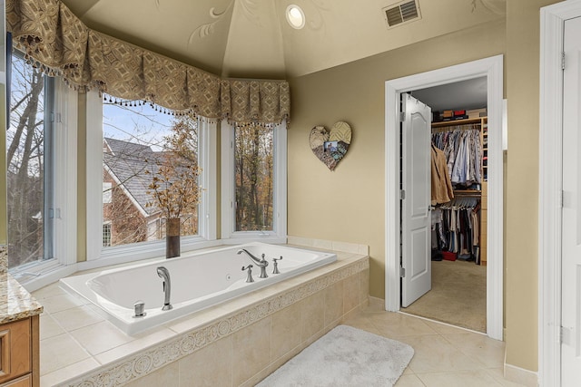 bathroom with tile patterned flooring, a relaxing tiled tub, and a healthy amount of sunlight