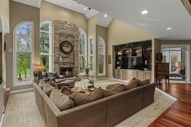 living room featuring a stone fireplace, plenty of natural light, and high vaulted ceiling