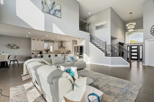 living room featuring dark hardwood / wood-style flooring, a towering ceiling, a healthy amount of sunlight, and an inviting chandelier