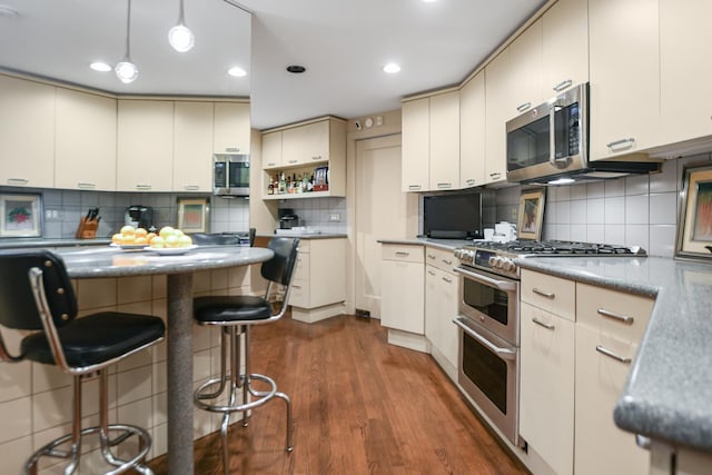 kitchen with dark wood-type flooring, a breakfast bar area, hanging light fixtures, stainless steel appliances, and decorative backsplash