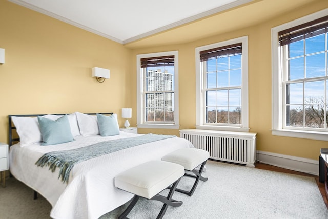 bedroom with ornamental molding, radiator heating unit, and wood-type flooring